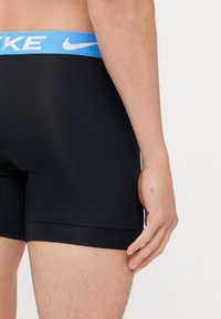 Čierne športové boxerky s modrým elastickým pásom, na ktorom je biele logo Nike. Hladká textúra a priliehavý strih, dĺžka do polovice stehna.