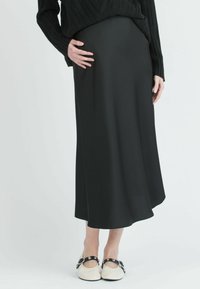 Musta satiini-midi-hame, jossa on sileä pinta ja A-linjainen siluetti, yhdistettynä vaaleanvärisiin kenkiin, joissa on koristeellisia osia.