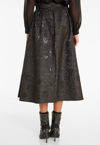 Zwarte bloemen brocade midi rok gedragen met een doorschijnende zwarte blouse en zwarte hoge hakken enkellaarsjes, gezien van achter.