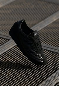 Pantofii sport negri cu un superior texturat, având o finisare netedă și elemente de design unghiulare. Sireturile și logo-ul sunt vizibile pe limbă.