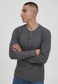 Szürke, hosszú ujjú henley póló, textúrált anyagból készült, kerek nyakú, elöl négy gombos gombolással.