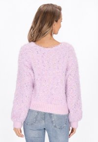 Lila flauschiger Pullover mit strukturiertem Finish, ausgestattet mit einem gerippten Taillenbund und Farbspritzern überall. Lange, lockere Ärmel.