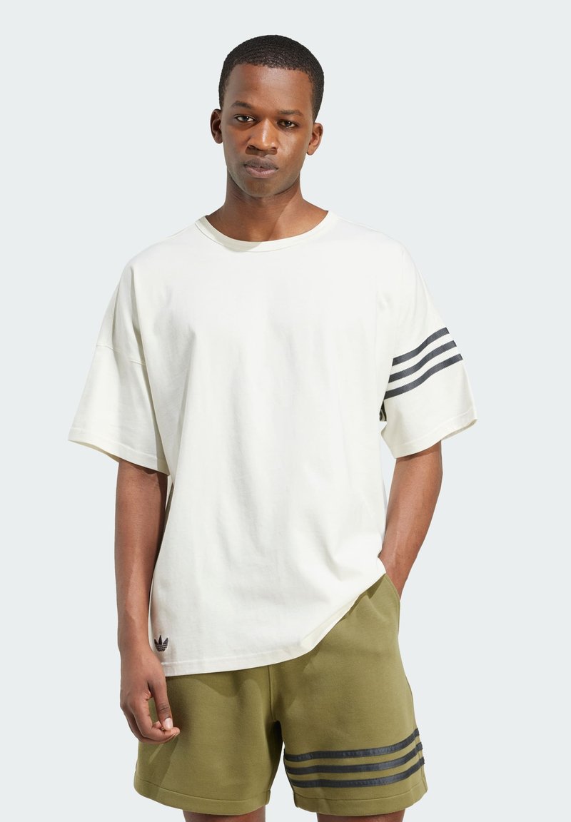 Krémové oversized tričko s kulatým výstřihem a krátkými rukávy, na levém rukávu s třemi tmavými pruhy a logem na lemu.
