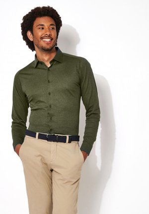 Langärmliges olivgrünes Hemd mit Button-down-Kragen, kombiniert mit beigen Hosen und einem marineblauen Gürtel, hat eine figurnahe Passform und eine weiche Textur.