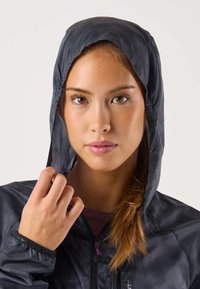 Giacca nera leggera con cappuccio, polsini elasticizzati e chiusura con coulisse, dalla texture liscia e con zip frontale.