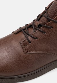 Stivali alla caviglia in pelle marrone con finitura testurizzata, design allacciato, cuciture rinforzate e suola in gomma per una maggiore durata.