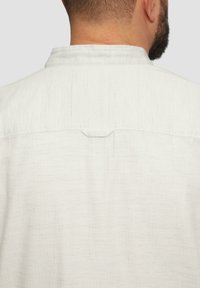 Witte textuurshirt met een achterkraag met horizontale strepen en een klein lusdetail bij de nek.