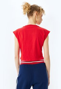 Rød cropped T-shirt med korte, strukturerede ærmer. Glat tekstur og simpel halsudskæring. Bæres sammen med marineblå bukser med en stribet talje.