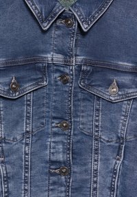 Jeansjacka i medelblått med en slitna finish. Har tryckknappar, två bröstfickor och en klassisk kragsdesign.