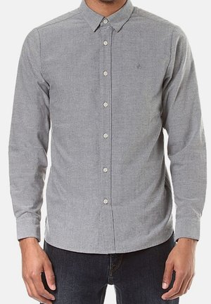 Man wearing a fitted long-sleeve button-up grey shirt with collar, standing with arms relaxed at sides, paired with dark jeans.