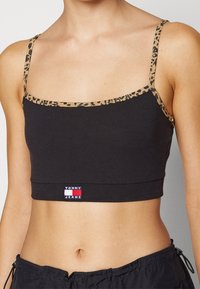Top corto nero con spalline a stampa leopardata, caratterizzato da un design aderente e una piccola etichetta con il logo "Tommy Jeans" all'orlo. Materiale in cotone morbido.