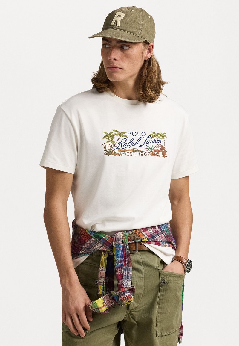Tricou alb din bumbac cu logo-ul brodat "Polo Ralph Lauren" și palmieri. Pantaloni scurți cargo de culoare verde măsliniu cu un obi din material cu un model multicolor legat în talie.