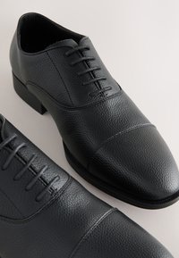 Schwarze Lederschuhe mit strukturierter Oberfläche, abgerundeter Spitze, Schnürdesign und niedrigem Blockabsatz. Kein sichtbares Markenlogo.