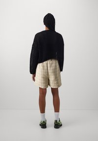 Czarny dzianinowy krótki sweter, beżowe szorty o teksturowym wzorze w kratę, białe skarpetki oraz czarne trampki z zielonymi akcentami.