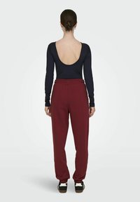 Bodysuit de manga larga en color navy con espalda baja, combinado con pantalones de chándal burdeos con cinturilla elástica. Zapatillas en blanco y negro completan el conjunto.