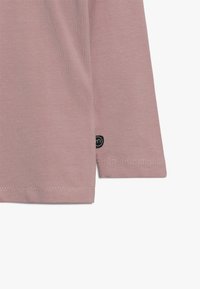 Jasnoróżowa, długosleeve koszula wykonana z miękkiego materiału, o prostym wzorze, z czarną metką logo z boku i starannie wykonanymi przeszyciami.
