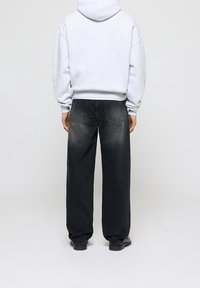 Sudadera gris con bolsillo canguro y corte holgado, combinada con vaqueros de pierna ancha desgastados en negro. Ambas prendas presentan una textura suave y casual.