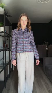 Szőtt tweed zakó lila, fehér és piros árnyalatokban, cipzáras elülső részével, strukturált gallérral és hosszú ujjaival. Lazább, világos nadrággal párosítva.