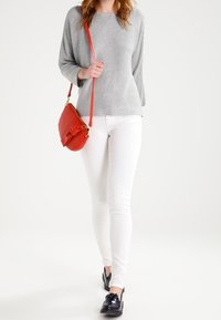 Grå stickad tröja med trekvartsärmar, vita tajta jeans och en röd crossbody-väska. Svarta snörskor fulländar outfiten.