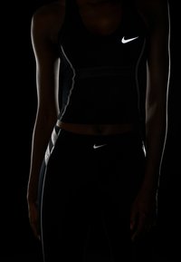 Czarny sportowy top na ramiączkach i legginsy z białym logo Nike. Posiada dopasowany krój, teksturę siatkową oraz odblaskowe akcenty.