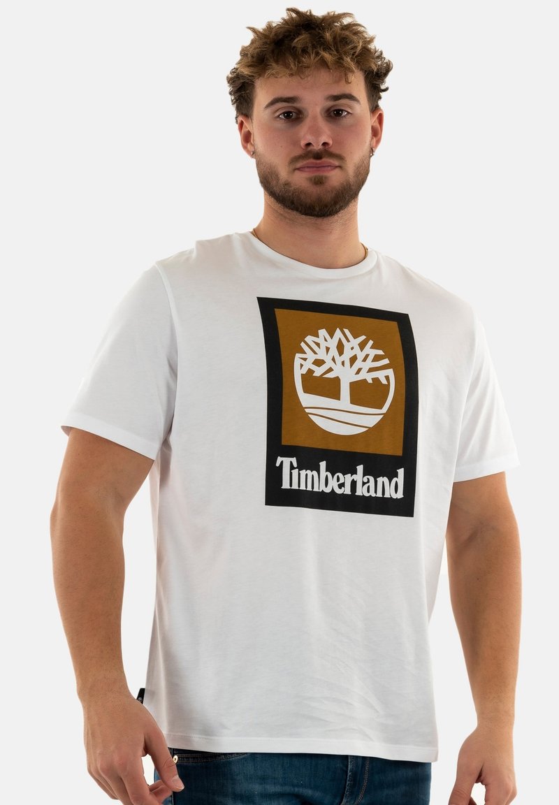 T-shirt bianco in cotone con scollatura rotonda, caratterizzata da una grande grafica del logo Timberland in marrone e nero centrata sulla parte anteriore.