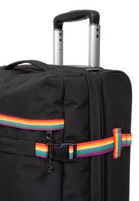 Bolso de viaje negro con dos asas retráctiles plateadas, que presenta una correa de arcoíris multicolor en la parte frontal con un detalle de hebilla negra.