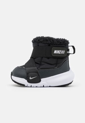 Sort og hvid Nike småbørnsstøvle med tyk sål, justerbare stropper, fleeceforing og Nike-logo på siden og stroppen.