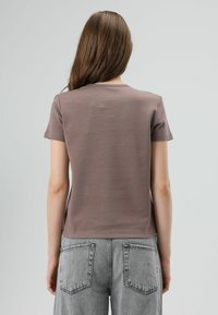 T-shirt met korte mouwen, aangesloten pasvorm in gedempt bruin, gladde stof, ronde hals, gecombineerd met grijze hooggetailleerde jeans met achterzakken.