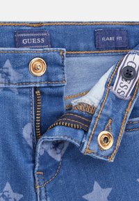 Jeans in denim blu con hardware dorato, dotati di zip e chiusura con bottone. Motivo a stelle visibile sul tessuto. Etichette del marchio visibili.