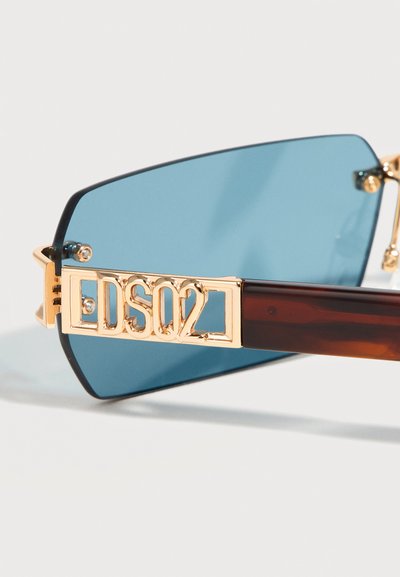 Ορθογώνιο φακός γυαλιών ηλίου με μπλε απόχρωση και χρυσλό λογότυπο DSQ2 στη σύνδεση του καφέ βραχίονα, σε ανοιχτό φόντο.