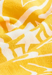 Sárga textil, amelynek textúrázott felülete merész fehér absztrakt mintákkal rendelkezik, gyönyörűen megdöntve a puhaságát és a vibráló színkontrasztot bemutatva.