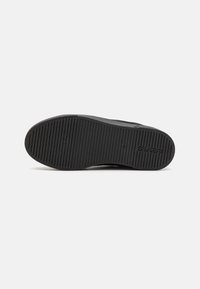Black rubber shoe sole with horizontal grooves, featuring a smooth edge and embossed lettering on the side. Flat design, durable texture.