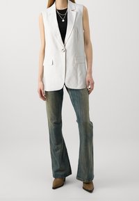 Bílý lněný bezrukávový blazer se dvěma předními kapsami, zapínání na jeden knoflík, kombinovaný s rozšířenými džíny a hnědými lodičkami se špičatou špičkou.