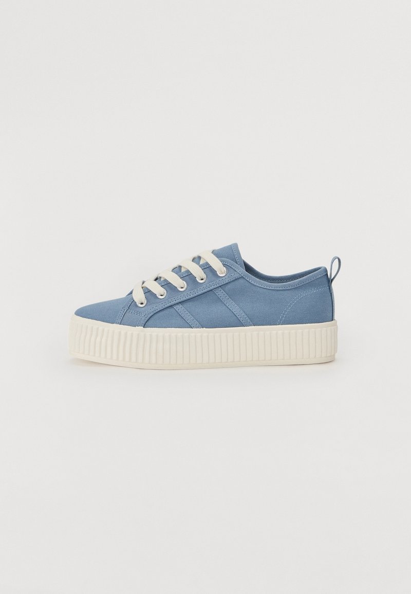 Basket basse bleue avec semelle blanche épaisse à nervures et lacets blancs sur un fond clair uni.