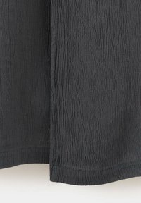 Gros plan d'un tissu noir à surface texturée et froissée avec des coutures visibles le long de l'ourlet.