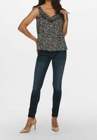 Top nero con stampa floreale, con spalline arricciate e scollatura a V, abbinato a jeans skinny scuri e tacchi nude. Design semplice e aderente.