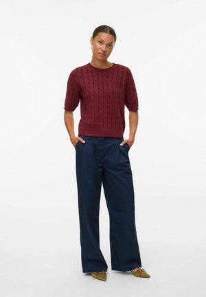 Bordeaux kabelstrikket sweater med korte ærmer, parret med marineblå vidde bukser og olivengrønne spidse flade sko. Enkel og struktureret design.
