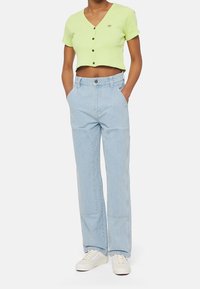 Grön kortärmad skjorta med knappar; ljusblå vida jeans; vita sneakers; har frontfickor och paneldetaljer.