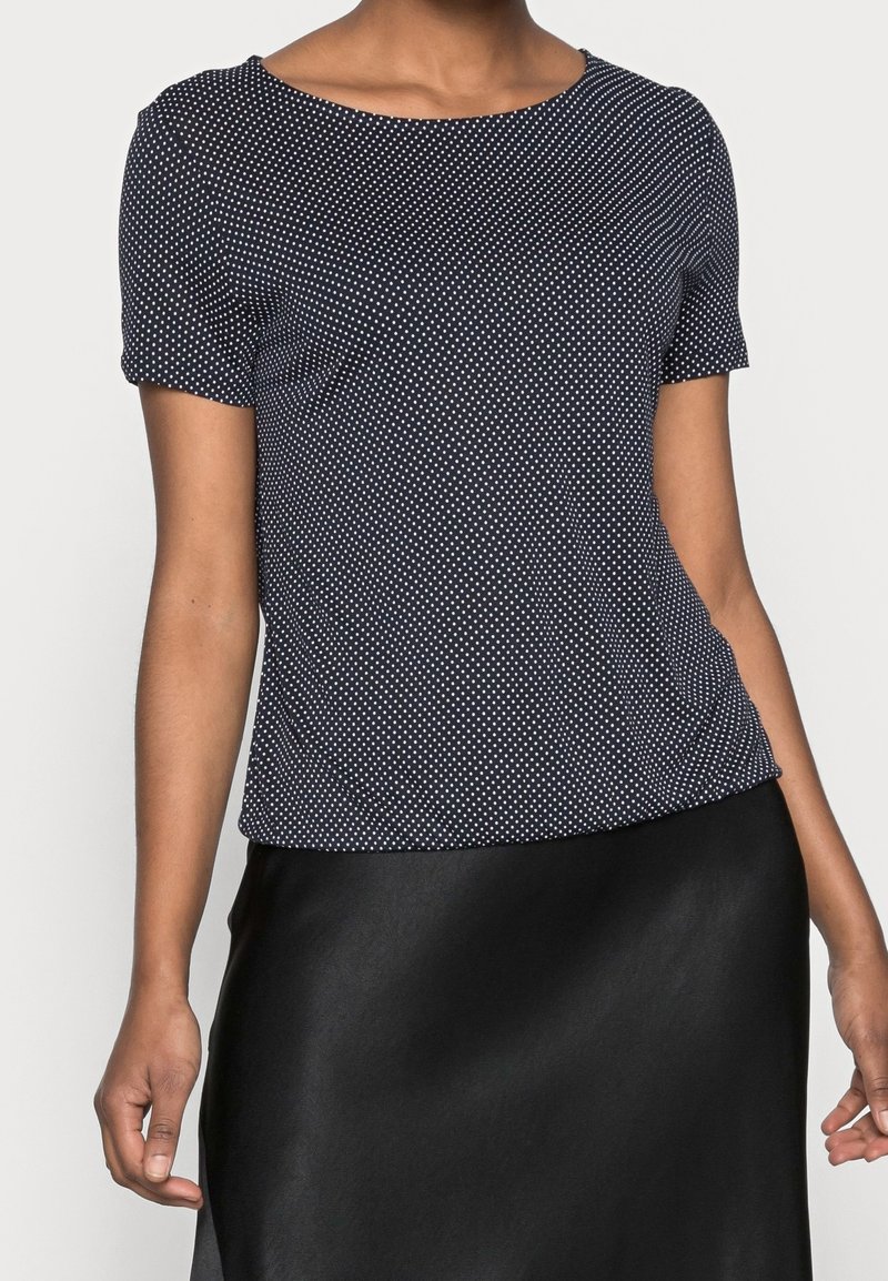 Marinblus med kort ärm och vita prickar, rund halsringning, slät textur och avslappnad passform. Matchad med en svart satinskjol nedan.