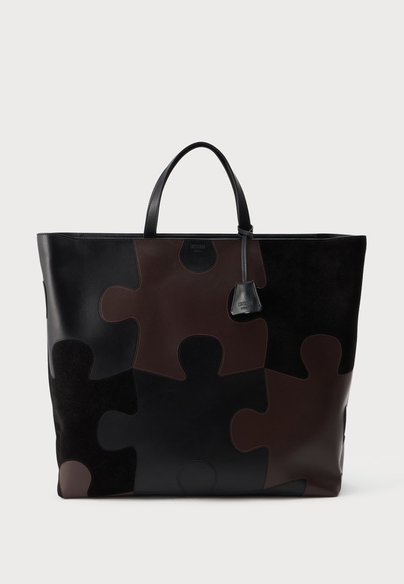 Grand sac cabas avec motif de pièces de puzzle en cuir noir et brun foncé et doubles poignées sur un fond clair uni.