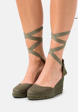 Olivew zielone espadryle na koturnie z płóciennym wierzchem i plecioną jute'ową podeszwą. Posiadają skrzyżowane paski wokół kostki dla pewnego dopasowania.