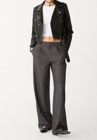 Veste motard courte en cuir noir avec garnitures en argent, associée à un pantalon large gris. Ballerines noires pointues avec détails cloutés.