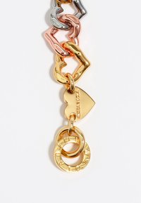 Cadenas de eslabones en oro, plata y oro rosa en varias formas, con un charm en forma de corazón y dos anillos grabados. Acabado de metal suave y brillante.