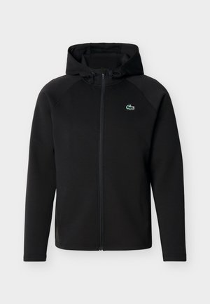 Μαύρη φούτερ ζακέτα με φερμουάρ, κουκούλα με κορδόνια και μικρό πράσινο λογότυπο κροκοδείλου στο αριστερό στήθος, παρουσιάζεται σε απλό λευκό φόντο.