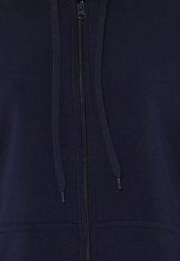 Marinblå zip-up hoodie med central dragkedja, ribbade detaljer och dragsnaran. Slätt tyg med kängurufickor fram.