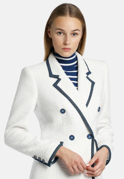 Witte gestructureerde blazer met marineblauwe accenten, dubbelzijdig met gouden knopen, met een getailleerd ontwerp en een contrasterende gestreepte coltrui eronder.