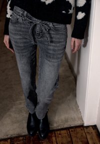 Pantaloni in denim grigio con una vestibilità rilassata, dotati di vita con coulisse e una leggera scoloritura. Abbinati a stivaletti neri alla caviglia.