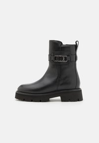 Bottine en cuir noir avec un bout rond, une semelle plateforme épaisse et une sangle décorative avec un détail de boucle circulaire.