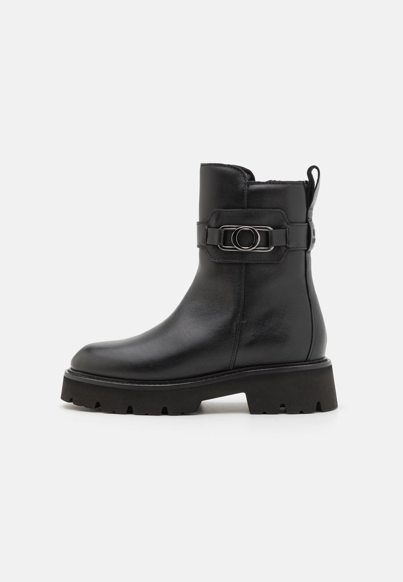 Bottine en cuir noir avec un bout rond, une semelle plateforme épaisse et une sangle décorative avec un détail de boucle circulaire.