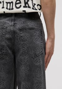 Grey denim pants with a floral pattern, featuring two back pockets. The fabric has a smooth texture and a subtle sheen.